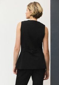 Svart ärmlös topp med en figurnära design, som har ett midjebälte i detalj. Slät tyg med en strukturerad siluett och en ren finish.