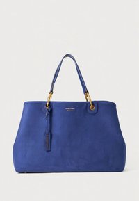 Mėlynas zomšos pirkinių krepšys su aukso spalvos furnitūra, dviem rankenomis, plokščiu pagrindu ir etikečių detalėmis. Švarus dizainas su lygiu paviršiumi ir be matomų raštų.
