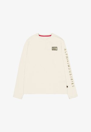 Košulja dugih rukava od kremaste pamučne tkanine sa crvenim unutrašnjim ovratnikom. Sadrži zakrpu s logotipom na prsima i natpis "ALPH INDUSTRIES" duž rukava.