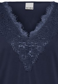 Haut en tissu bleu marine avec encolure en V, orné d'une délicate bordure en dentelle florale dans une teinte bleu marine assortie.
