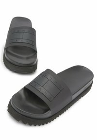 Black rubber slide sandals with textured strap featuring embossed "TOMMY JEANS" logo and a thick, ridged outsole for grip.