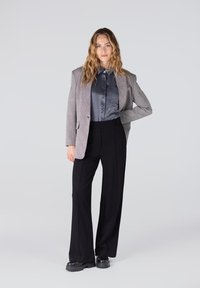 Grijs gemêleerd blazer over een satijnen grijze shirt, gecombineerd met aangesloten zwarte broeken en zwarte plateau schoenen. Soepele texturen en een op maat gemaakte pasvorm.