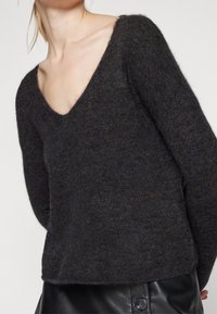Mörkgrå stickad tröja med djup V-hals, långa ärmar och en avslappnad passform. Tillverkad av mjukt, texturerat tyg och har ett subtilt melerat mönster.