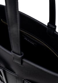 Borsa a tracolla nera in pelle liscia con zip dorata. Presenta manici doppi e un'etichetta interna. Design minimalista con forma strutturata.