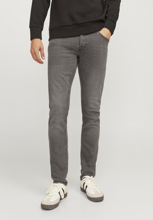 Gray slim-fit jeans with five pockets, belt loops, and subtle fading. Paired with white sneakers featuring black stripes.