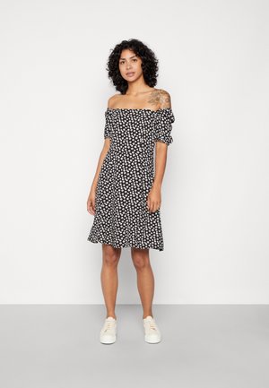 Vestido preto sem ombros com um pequeno padrão floral branco, mangas curtas bufantes e saia rodada. Combinado com sapatilhas brancas.