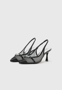Mustat verkkomaiset slingback-korkokengät, joissa on terävä kärki, ohuet hihnat ja pieni koristeellinen hopeinen yksityiskohta. Teksturoitu verkkomateriaali ylhäällä ja kapea korko.