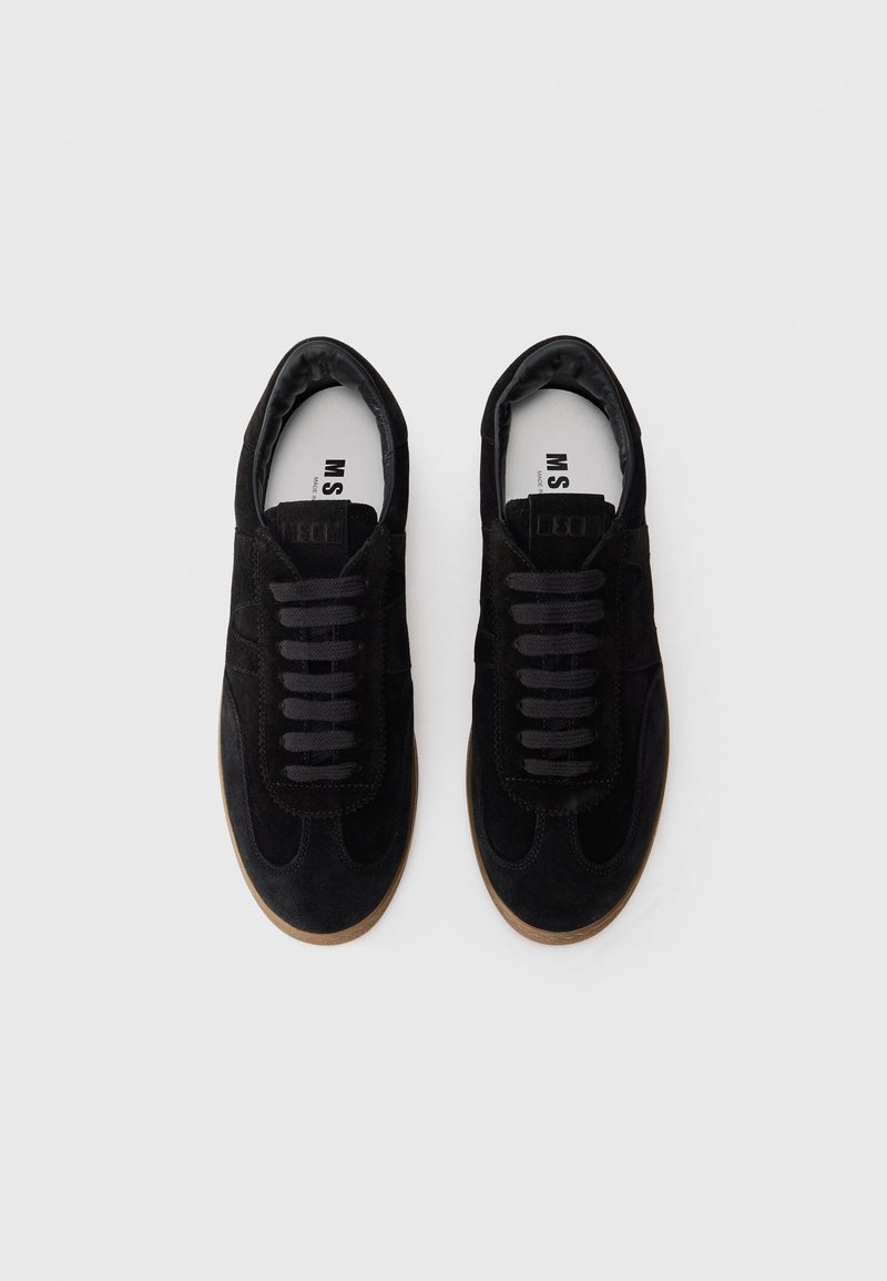 Baskets en suède noir avec un bout rond, des lacets plats et une semelle en caoutchouc texturée. L'intérieur présente un revêtement doux. Branding minimal visible.