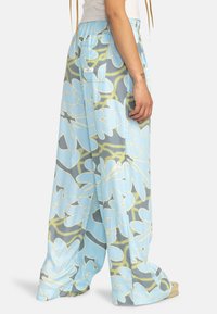 Pantalons larges bleu clair avec de grands motifs floraux en blanc et vert. Fabriqués à partir d'un matériau doux avec une taille élastique et des poches latérales.