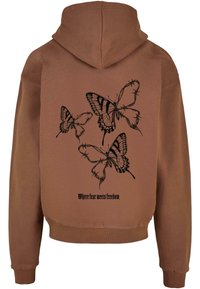 Sweat à capuche marron avec trois papillons noirs enveloppés dans du fil barbelé et le texte « Où la peur rencontre la liberté » dans le dos.