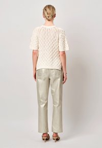 Crème gebreide trui met een textuurpatroon, gecombineerd met lichtmetalen zilveren broek, die een relaxed fit en een lengte tot halverwege de kuiten heeft.