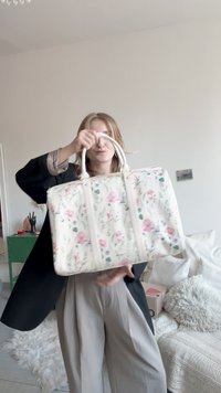 Kremo spalvos rankinė su gėlių raštais, pagaminta iš tvirto audinio. Turi dvi rankenas ir užtrauktuką, puošta rožiniais ir žaliais botaniniais raštais.