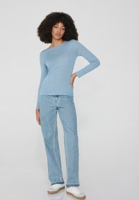 Helles blaues Langarmoberteil mit Bootsausschnitt, kombiniert mit hellen Jeans. Lässiger Stil mit schlanker Passform und weicher Textur. Weiße Sneaker.