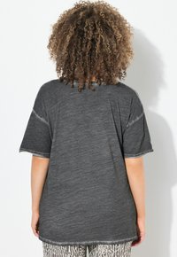 Tmavě šedé oversized tričko s kulatým výstřihem a krátkými rukávy. Měkká, texturovaná tkanina s roztrhaným lemem a kontrastními švy.