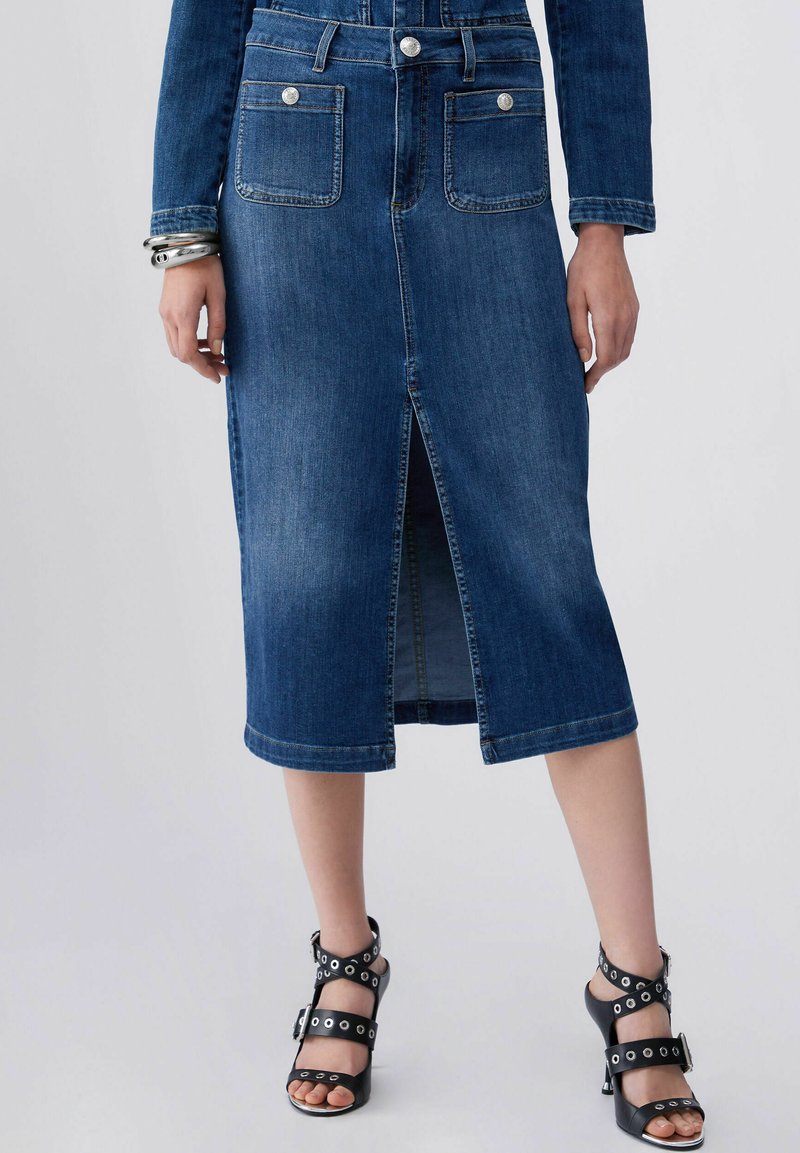 Denim midi skirt with front slit, silver button details, worn with black strappy high-heeled sandals and silver bracelets on left wrist.