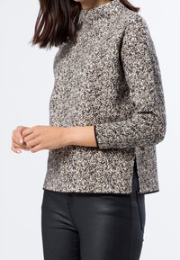 Suéter de manga larga en un patrón moteado negro y beige, con cuello alto y aberturas laterales, hecho de una tela de punto texturizada.