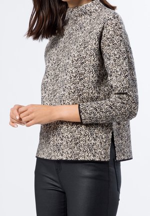 Pull à manches longues en tricot avec un motif moucheté noir et beige, doté d'un col montant et d'entailles sur les côtés, fabriqué en tissu tricoté texturé.
