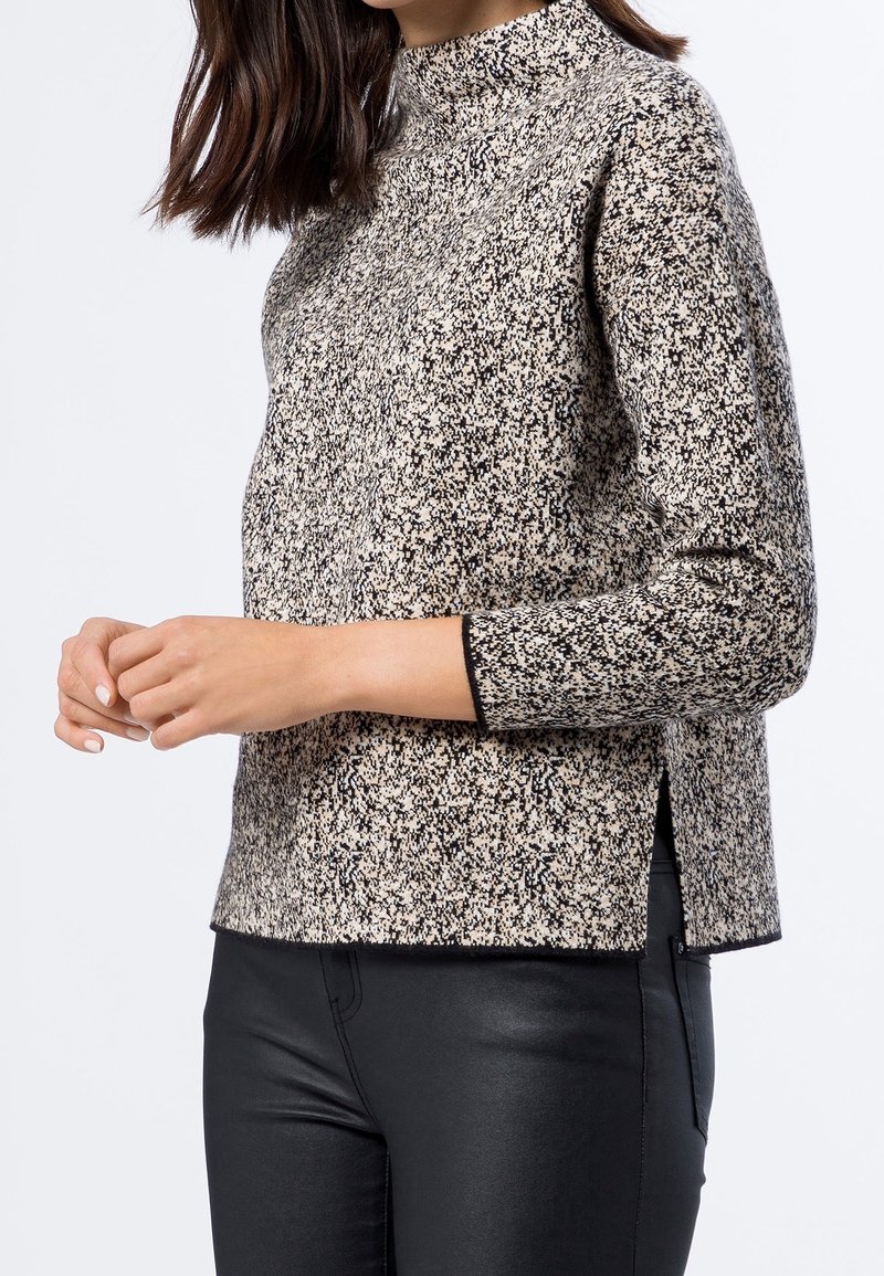 Suéter de manga larga en un patrón moteado negro y beige, con cuello alto y aberturas laterales, hecho de una tela de punto texturizada.
