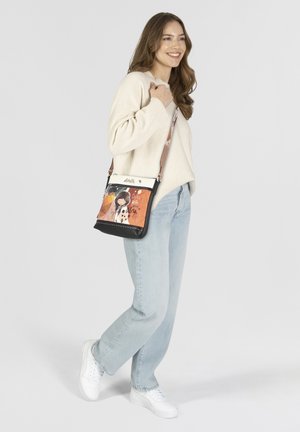 Sac bandoulière en matière synthétique, avec un motif graphique et une base noire sur le dessus blanc. Sangle ajustable et fermeture éclair.