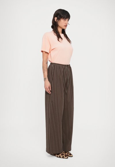 Ροδακινί κοντομάνικη μπλούζα συνδυασμένη με καφέ ριγέ παντελόνια με φαρδιά πόδια. Τα παντελόνια διαθέτουν ελαστική μέση με κορδόνι και ολοκληρώνονται με παπούτσια με λεοπάρ μοτίβο.