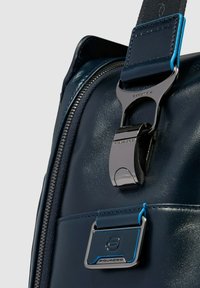 Marineblauer Rucksack aus glänzendem, synthetischem Material mit einer metallischen Schnalle und kontrastierenden hellblauen Akzenten. Verschluss mit Reißverschluss sichtbar.