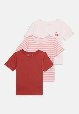 Trois t-shirts enfants à manches courtes empilés, les couleurs incluent rouge rouille uni, rayures roses et blanches, et rose pâle avec un petit motif cerise.