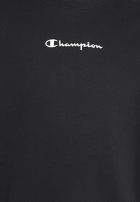 Svart bomulls t-shirt med en vit "Champion"-logotyp över bröstet. Tyget har en slät textur och en klassisk rundad halsringning.