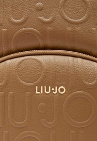 Zaino in pelle marrone con texture, caratterizzato da un logo "LIU•JO" impresso e motivi circolari, con dettagli della cerniera in tono oro.