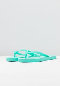 Turquoise flip-flops made of rubber with a textured strap and a flat sole featuring a wavy edge pattern for traction.