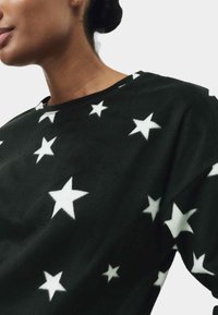 Zwarte fleece sweatshirt met een wit sterrenpatroon, ronde hals en een relaxed fit. De textuur lijkt zacht en iets pluizig.
