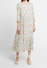 Robe midi florale à manches 3/4, avec une base blanche, des motifs roses et verts, un col rond et un tissu froncé à la taille.