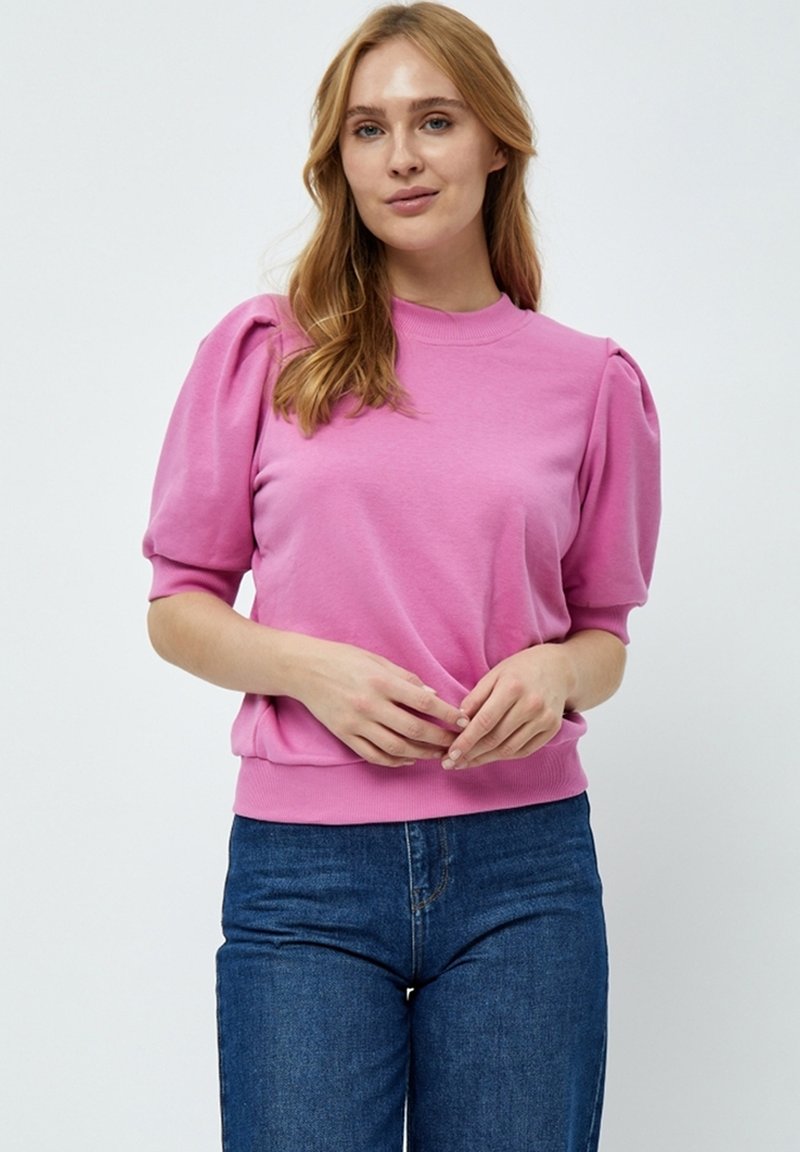 Rosa lätt stickad tröja med korta puffärmar, ribbad halsringning och nederkant, tillsammans med blå jeans. Slät tygtextur, avslappnad passform.