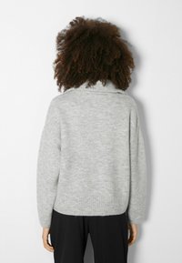 Suéter de lana gris con un alto cuello acanalado, hombros caídos y dobladillo acanalado. Textura suave y ajuste relajado.