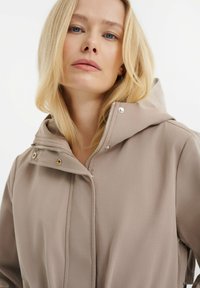 Beige leichte Jacke mit Kapuze, ausgestattet mit einem Frontreißverschluss, Druckknöpfen und einer glatten, matten Textur. Akzente umfassen silberne Hardware.