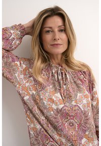 Blouse à manches longues ornée d'un motif cachemire multicolore. Fabriquée en tissu léger avec un col froncé et des poignets élastiques.