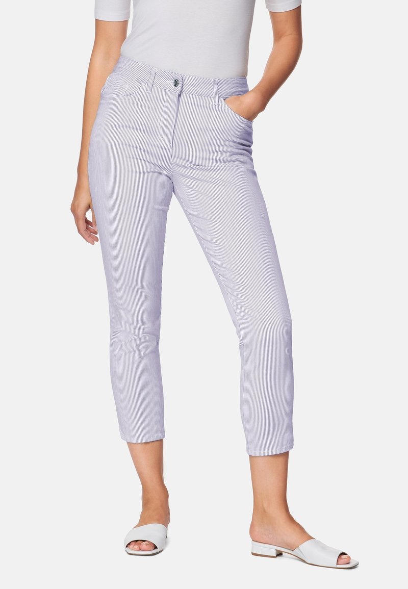 Femme portant un pantalon court rayé blanc et bleu clair avec des poches, associé à des chaussures blanches à bout ouvert et un haut blanc.