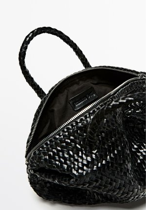 Borsa a tracolla nera intrecciata con manici intrecciati, chiusura con zip e interno in tessuto nero con etichetta del marchio. Texture liscia e forma strutturata.