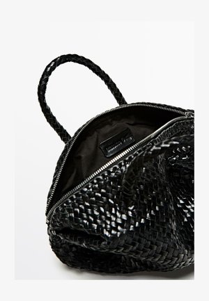 Sac à main tressé noir avec poignées tressées, fermeture éclair et un intérieur en tissu noir comportant une étiquette de marque. Texture lisse et forme structurée.