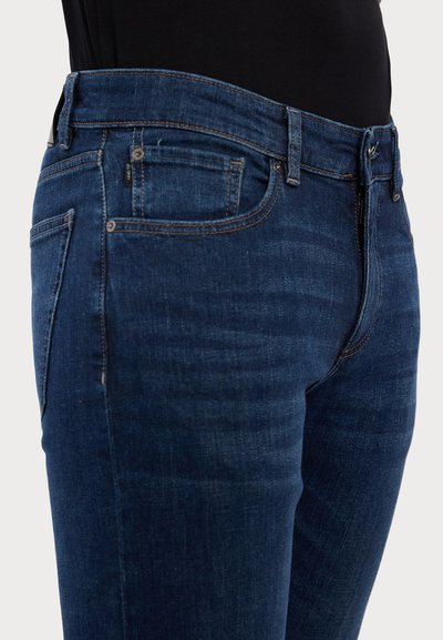 Dark blue denim jeans with a slim fit, featuring five pockets, contrast stitching, and a smooth texture. Zippered fly and belt loops included.