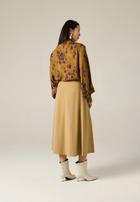 Blusa gialla con motivo floreale viola, abbinata a una gonna midi beige e stivaletti bianchi. Tessuto liscio con design a vestibilità ampia.