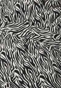 Tecido com padrão de zebra em preto e branco, com uma textura suave, apresentando linhas onduladas que criam um padrão dinâmico. O tecido forma pregas na cintura.