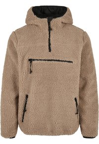 Pullover in pile tan con colletto alto, zip frontale a metà e tre tasche con zip. Tessuto morbido e testurizzato con dettagli neri.