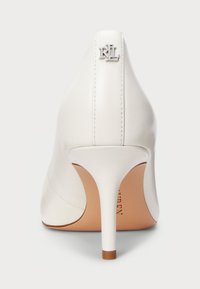 Fehér, magas sarkú cipő, hegyes orral, sima bőrből készült felsőrésszel és ezüst logóval a hátsó sarkán.