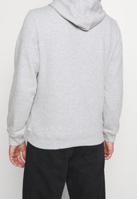 Sudadera con capucha gris de corte relajado, con puños y dobladillo acanalados. Presenta una textura suave, bolsillo canguro y una composición de tela suave.