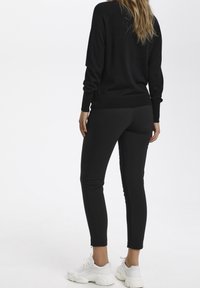 Svart stickad tröja med långa ärmar, tillsammans med slim-fit svarta byxor med ankelsiddragkedjor och vita sneakers. Enkelt och monokromatiskt design.