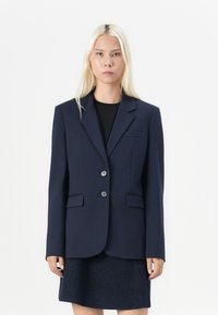 Navyblauwe op maat gemaakte blazer, enkelknopsluiting, twee knopen, reverskraag, voorzakken, gestructureerde stof en een gladde afwerking.