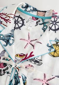 Valge öösärgi ülaosa, millel on mereteemaline mustriga kalad, meritähed ja roolirattad, rõhutatud helesinise krae ja paelaga.