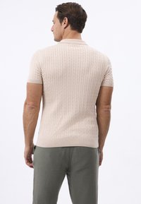 Camisa polo de punto de manga corta en beige claro con patrón de trenzado, cuello y dobladillo acanalados. Combinada con pantalones verdes de corte holgado.