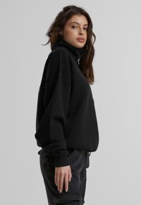 Svart genser med høy krage, avslappet passform og lange ermer. Materialet ser mykt ut med en jevn tekstur og minimal detaljering.