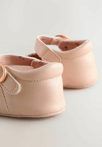 Sanfte rosa Babyschuhe mit einer glänzenden roségoldenen Schnalle, die über ein glattes Lederäußeres und eine genähte Sohle verfügen, auf einem hellen Hintergrund platziert.